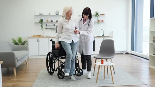Doctor Helping Senior Woman from Wheelchair in Home