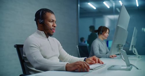 African American Hotline Operator Talks on Headset with Customer Works on Computer