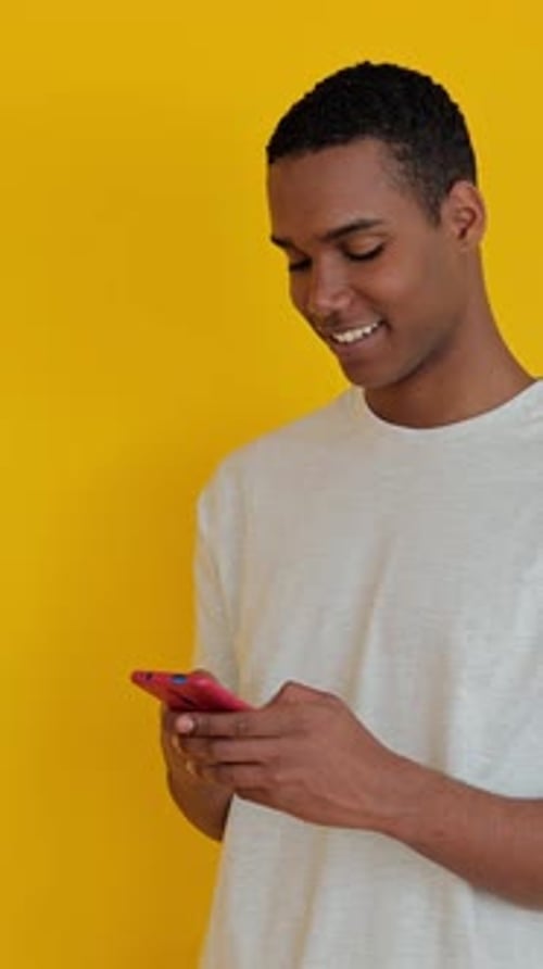Young Adult Using Smartphone Against Yellow Background