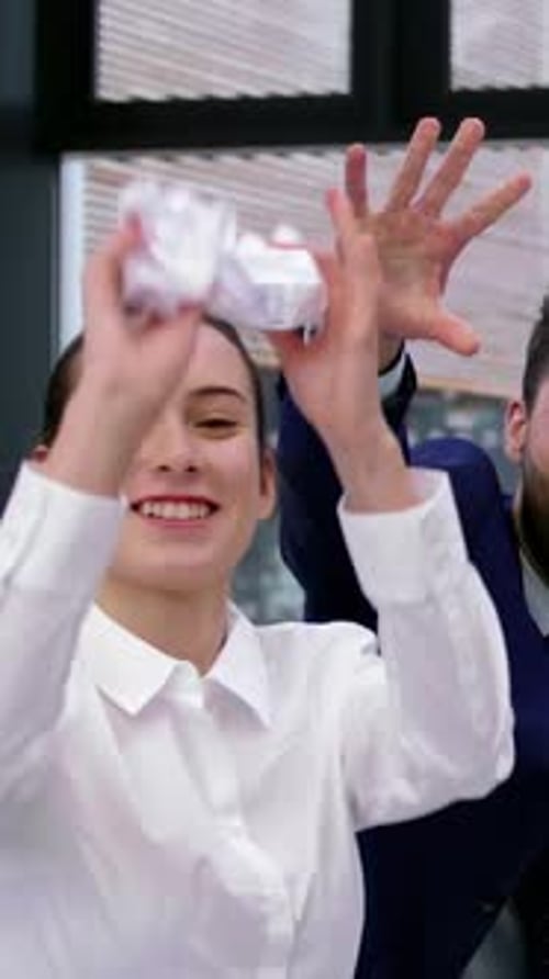 Mulher com camisa de escritório jogando papel amassado após colega estendendo a mão, iluminando o clima de negócios