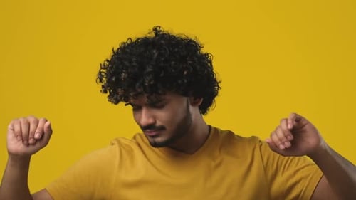 Young Indian Bearded Guy with Curly Hair Wearing Tshirt Dancing Over Orange Studio Background