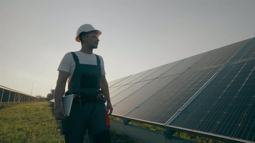 A Worker Walks Through a Solar Panel Station Analyzing Their Performance