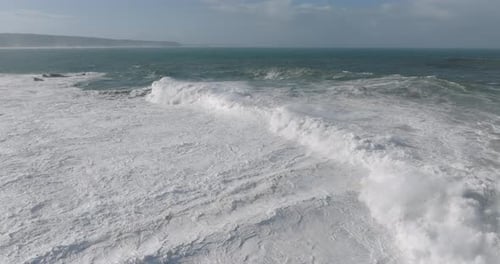 Aerial drone shot of big waves coming into shore on a day with giant waves in Nazaré, Portugal,