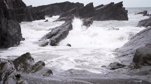 Powerful Ocean Waves Crashing Against Jagged Dark Coastal Rock Formations