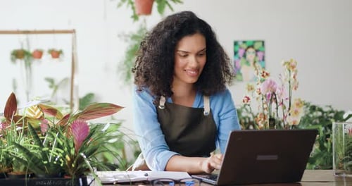 Young African American woman flower business owner in apron using laptop working at the floral store