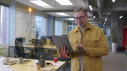 Male Manager Standing in Office Holding Laptop and Smiling