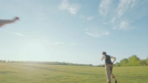 Young Lively Couple Running through Sunlit Meadow and Playing Tag