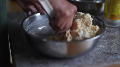 Raw dough ingredients mixed using baking spoon in steel bowl on kitchen tabletop, filmed as closeup
