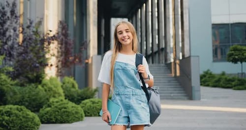 Porträt eines lächelnden Schulmädchens mit Schultasche und Buch, das beim Gehen nach der Schule in die Kamera schaut