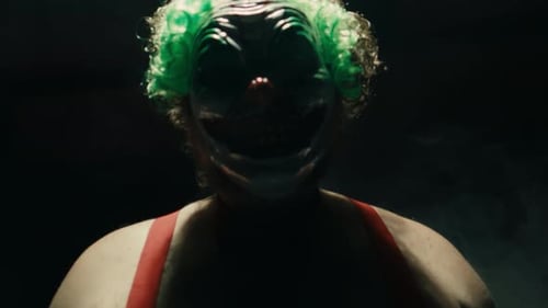 Scary Man in the Horror Clown Mask with Green Hair Standing in Suspenders in the Dark Studio and