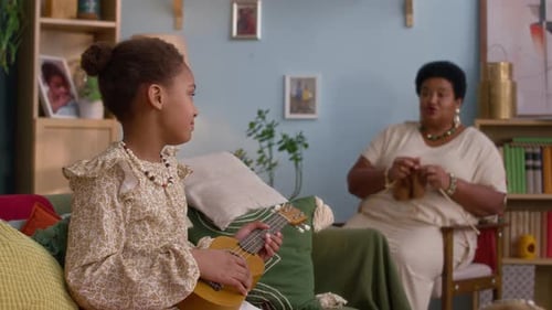 Girl Plays Ukulele with Grandmother Knitting at Home