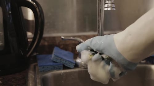 A Hand Squeezing A Dishwashing Sponge In The Kitchen Sink - Close Up Shot