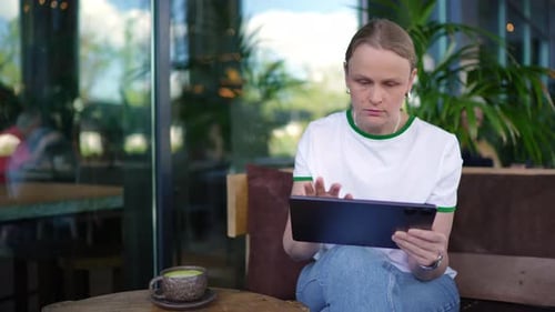 Woman Drinking Coffee and Using Tablet in Outdoor Cafe