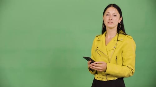 A Young Beautiful Caucasian Woman Holds a Smartphone and Talks to the Camera Green Screen Studio