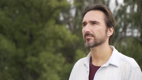 Un bel homme caucasien regarde au loin dans les arbres de pensée en arrière-plan flou en gros plan
