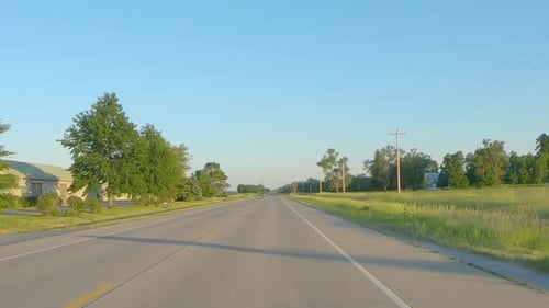 POV while driving on a country highway past farms and fields; landscape is very flat