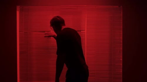 Portrait of Male Model in Dark Studio Young Man in Tshirt Standing Near Window with Red Light Behind