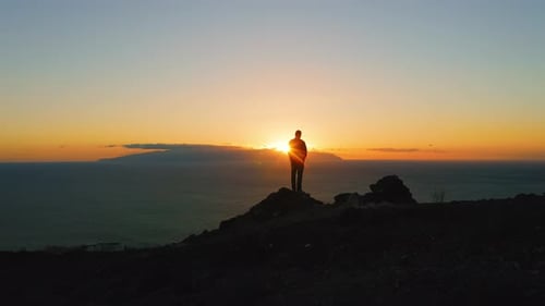Man Standing on Top of Rock with Epic Mountain Viewpoint and Enjoying Colorful Sunset Light Flare