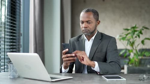 Focused Man Using Phone at Desk in Office