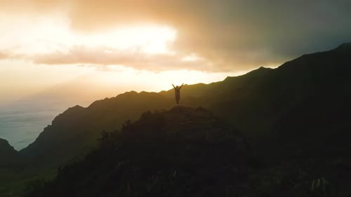 Lonely Girl Stands on Top of Rock Mountain Ocean Background at Sunset