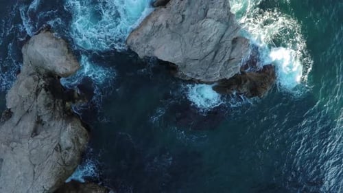Waves Crash Powerfully Against Rugged Coastal Rocks in Aerial View