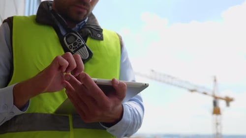 Arquiteto masculino usando capacete no canteiro de obras enquanto trabalha em um tablet digital