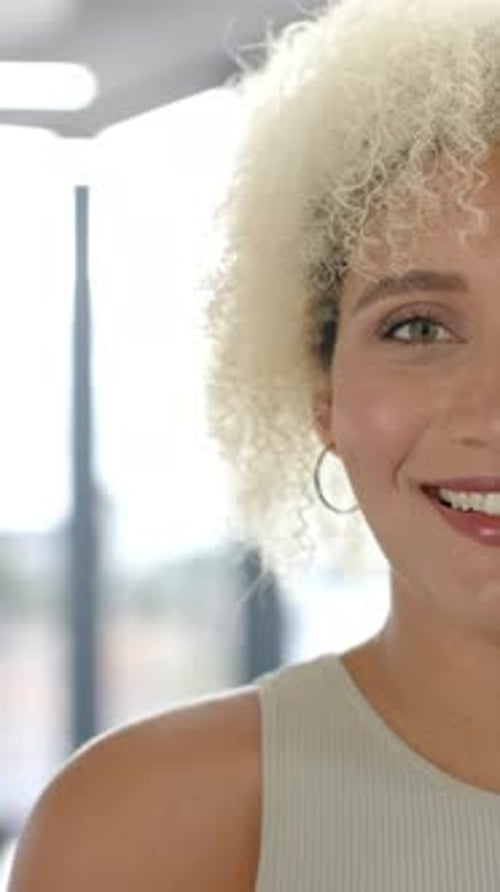 Vidéo verticale : Femme souriante aux cheveux bouclés regardant la caméra dans un bureau lumineux