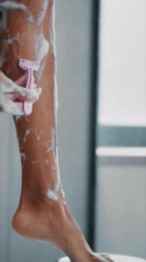 Woman Shaving Leg in Bright Bathroom