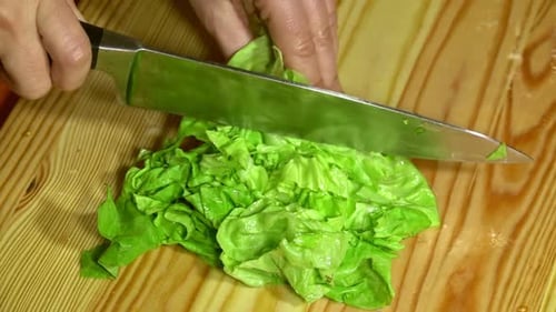 Knife cuts the lettuce in kitchen on wooden board. Close up.