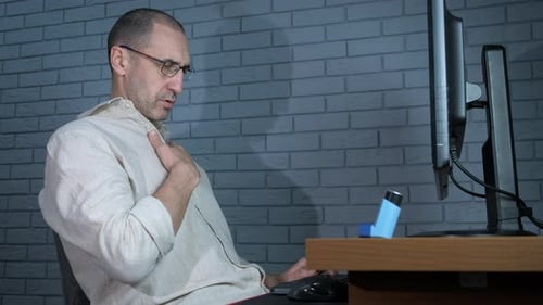 Man Using Inhaler at Computer at His Desk