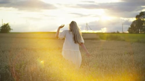 A Beautiful Woman Walks Through a Wheat Field at Sunset