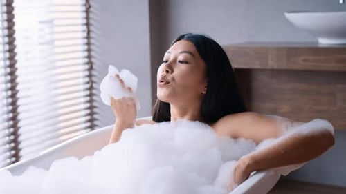 Woman Relaxing in a Bubble Bath Blowing Foam