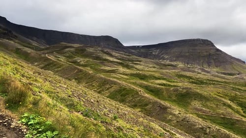 Lush green Icelandic valley with imposing basalt mountains under cloudy skies, daylight shot