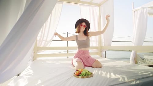 A Woman is Relaxing and Dancing at a Beach Cabana Feeling Carefree and Content While Savoring Fruits