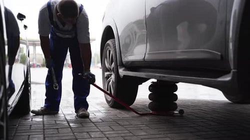 Auto Mechanic Uses Hydraulic Jack to Lift Car for Tire Change at Garage Man in Uniform Services