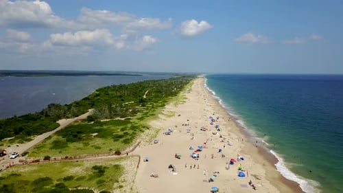 Drone shot moving forward of Atlantic Ocean and bay with shore houses, beach, boats, and boardwalk.