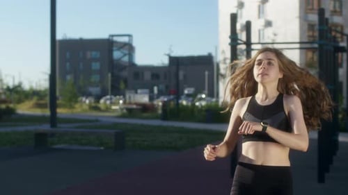 Young Woman with Curly Hair Run in Frame and Goes in for Sports on Street and Looks at Her Watch