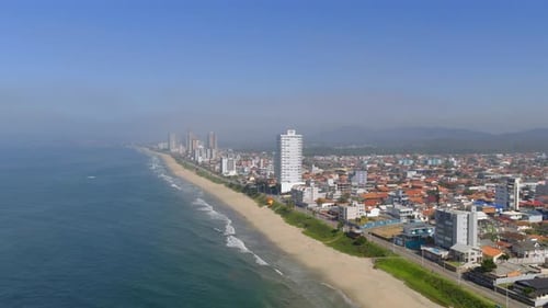 Upward panorama drone fly of coastline with sandy beach and local buildings lined along oceanfront,