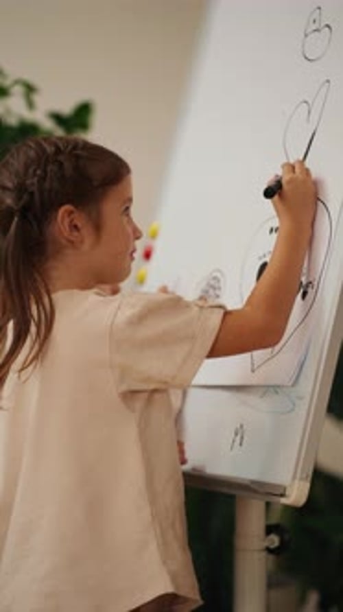 Vertical Video of a Girl in a White Tshirt Drawing with a Black Marker on a Large Sheet of Paper