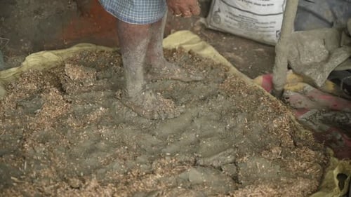 Adult Using Feet to Mix Mud with Straw