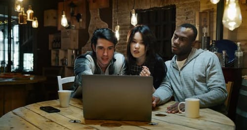 Slow motion of young college friends using a laptop together for study project and drinking tea in