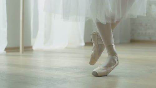 Close-up Shot of Ballerina's Legs. She Dances on Her Pointe Ballet Shoes. She's Wearing White Tutu