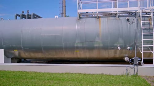 Large cylindrical metal tank with rust stains and access ladder at industrial plant