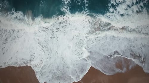 Cinematic Aerial View Of Crashing White Waves Against The Shoreline