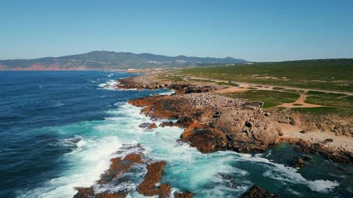 Stormy waves crashing on rocky beach cliffs in sunny coastal ocean aerial view