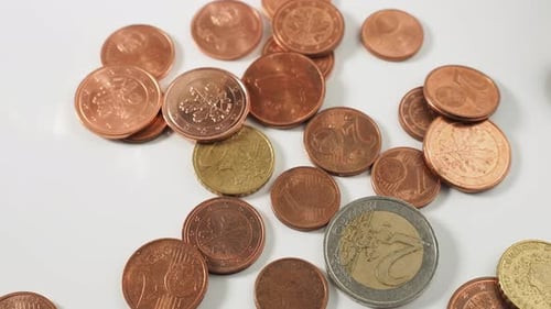 Close-up of metal coins falling on a white table. Eurocents spill out on the table.