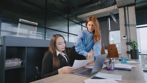Professional Women Collaborating at Desk with Laptop in Office