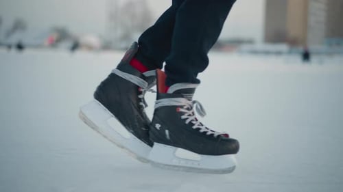 Leg View of Person Skating Past Another on Frozen Ice Rink Under Winter Light