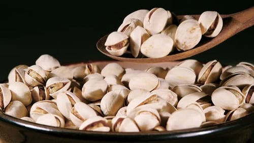 Dried Pistachio Nuts with Cracked Shells and Green Kernels Falling into a Rustic Ceramic Bowl