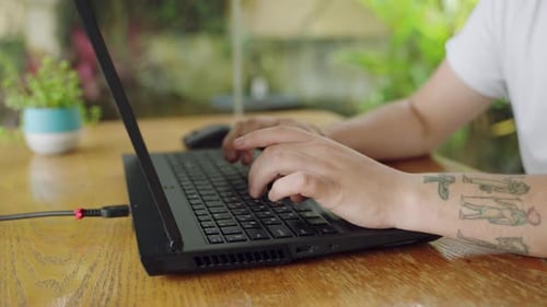 Un développeur tatoué tape du code sur un ordinateur portable dans un café chaleureux dédié au travail : les doigts bougent rapidement